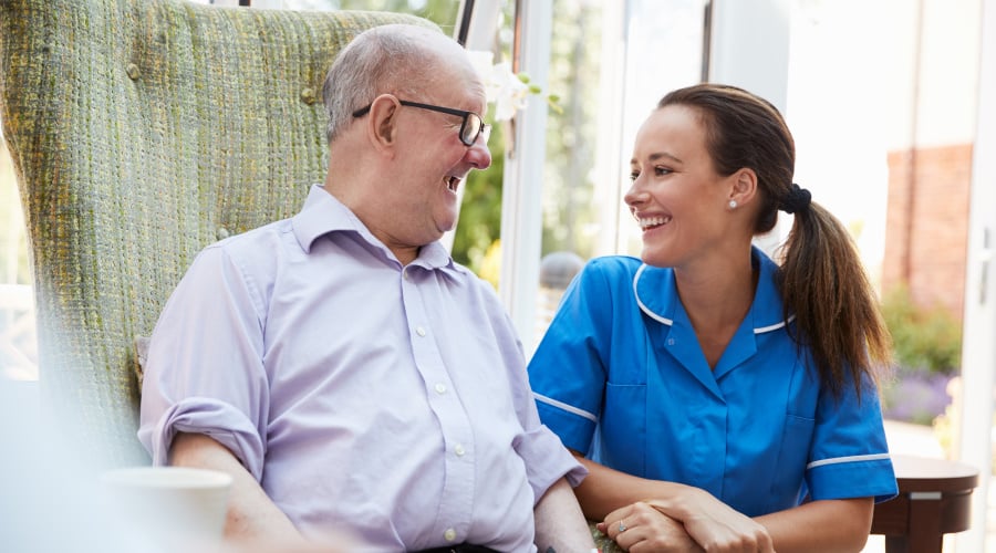 nurse sitting with man with glasses and a purple shirt both are smiling